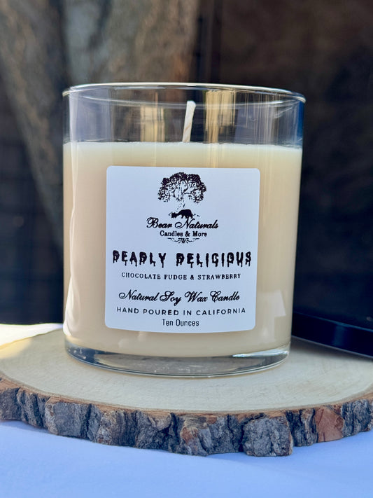 A ten ounce white scented candle in a clear glass jar with a black metal lid and white label with black writing sitting on a wooden surface. The candle is called "Deadly Delicious".