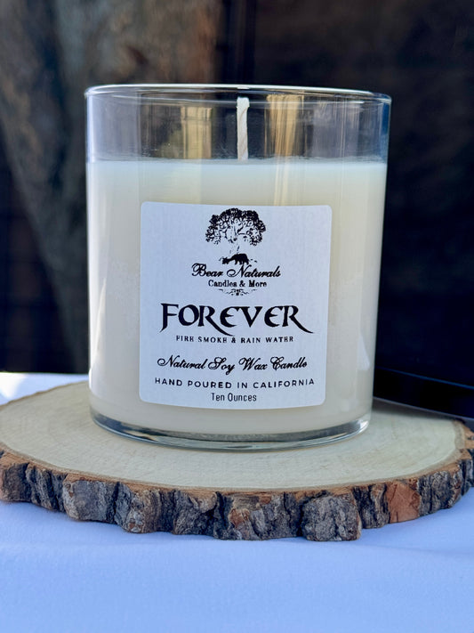 A white ten ounce candle in a clear glass jar with a black metal lid and white label with black writing sitting on a wooden surface. The candle is called "Forever".