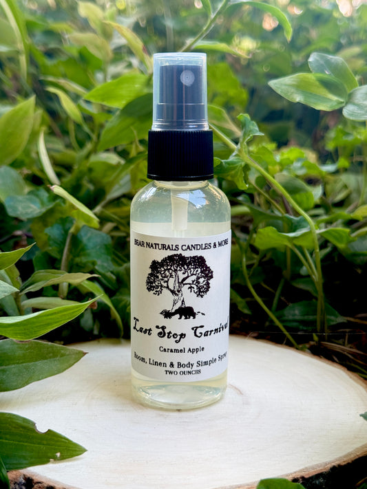 A clear two ounce finger-tip spray bottle with black and white label on a wooden surface with green leaves in the background. The bottle contains the scent "Last Stop Carnival".
