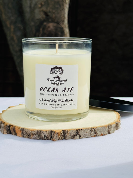 A white ten ounce candle in a clear glass jar with a black metal lid and white label with black writing sitting on a wooden surface. The candle is called "Ocean Air".