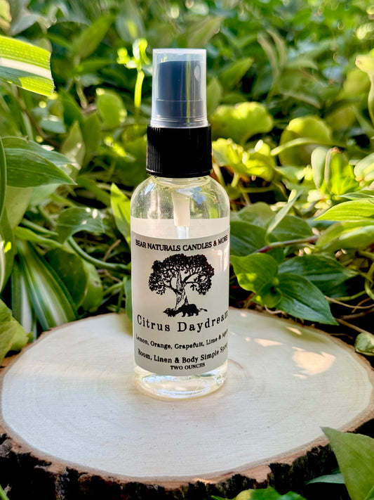A Clear two ounce finger-tip spray bottle with black and white label on a wooden surface with green leaves in the background. The bottle contains the scent "Citrus Daydream".