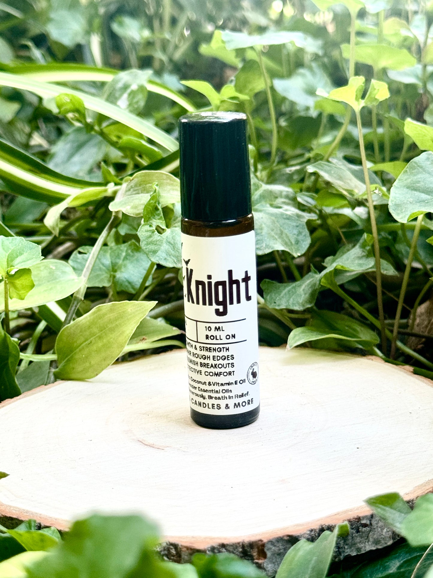 10ml amber colored roll on bottle with a black lid featuring a white label reading "Dark Knight All Natural Beard Oil" sitting on a wooden surface with green leaves in the background