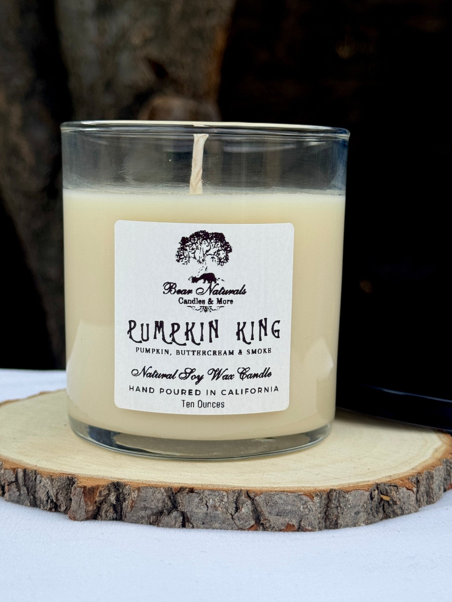 A white ten ounce candle in a clear glass jar with a black metal lid and white label with black writing sitting on a wooden surface. The candle is called "Pumpkin King".