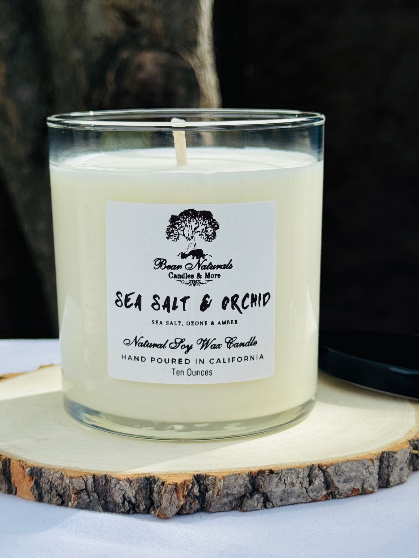 A white ten ounce candle in a clear glass jar with a black metal lid and white label with black writing sitting on a wooden surface. The candle is called "Sea Salt & Orchid".
